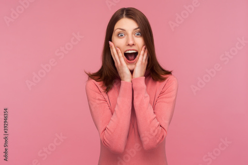Extremely shocked surprised woman with brown hair screaming holding hands on cheeks, cant believe in her victory, astonishment. Indoor studio shot isolated on pink background