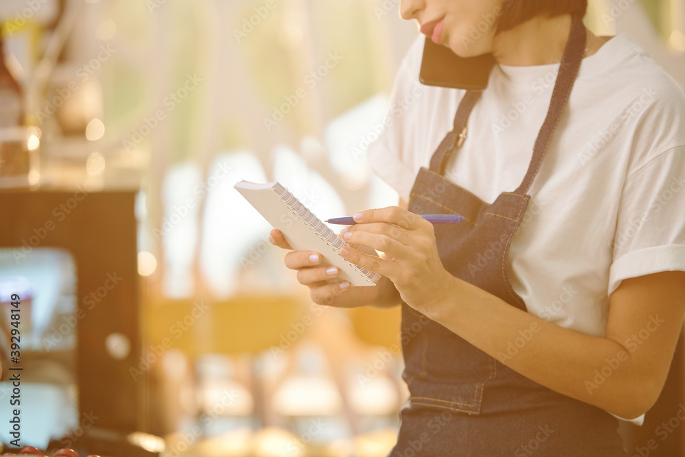 Obraz premium Cropped image of female barista or waitress talking on phone wih customer and discussing delivery details