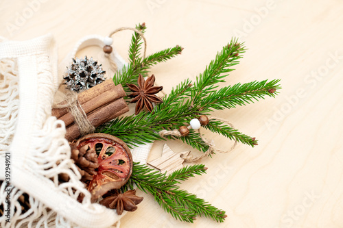 Spruce branch in an ecological string bag made of cotton and Christmas decorations on a wooden background. Assortment of cozy hygge Xmas. DIY, zero waste, eco friendly. Flat lay, top view.