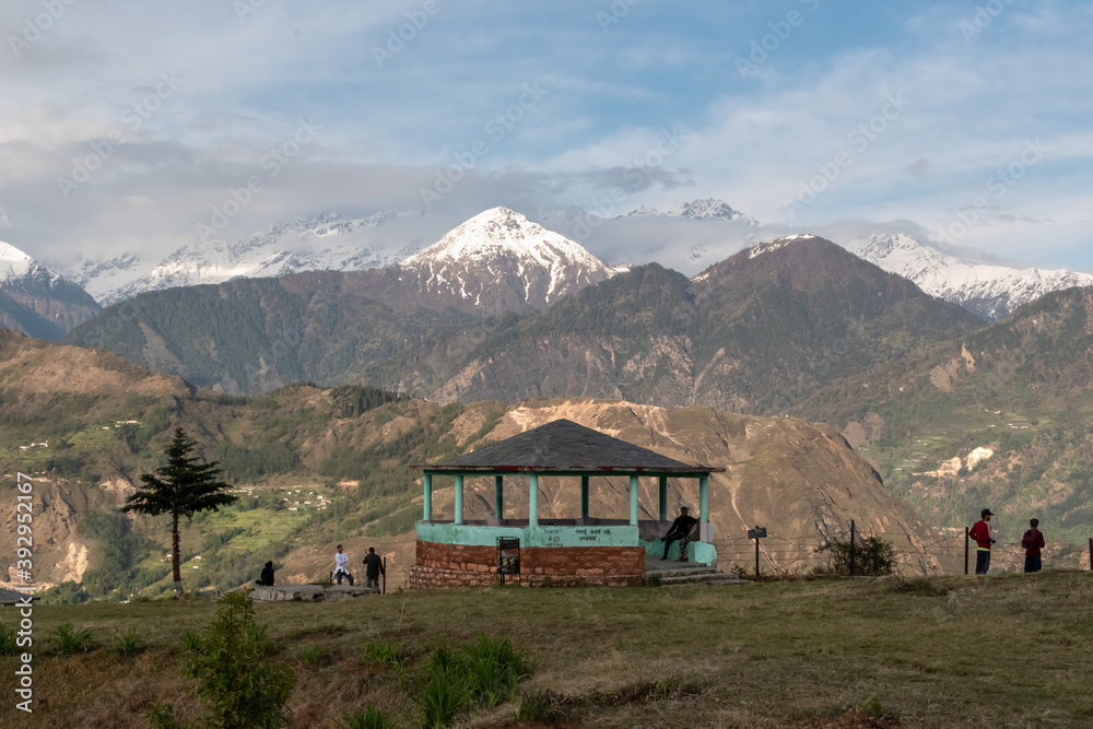 A viewpoint at the edge of a green meadow with a view of the snow capped Himalayan mountain peak of the Panchachuli range.