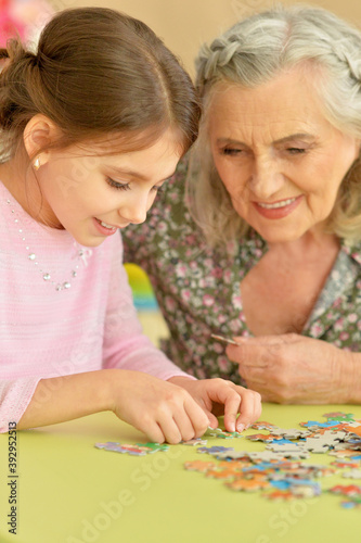 Cute little granddaughter and grandmother collecting puzzles together at home
