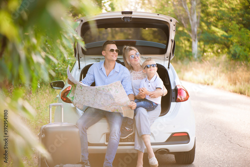 A man a woman and a child of four years in the woods next to the car is ready to travel and choose a place on the map where to go © nagaets