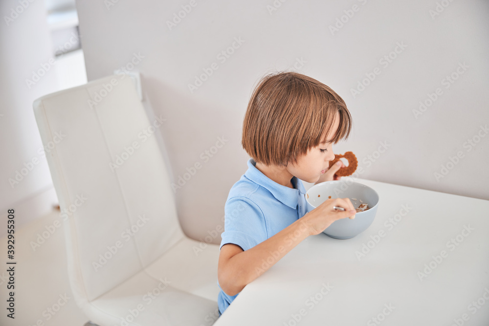 Lovely child having breakfast at a white kitchen table Lovely child having breakfast at a white kitchen table