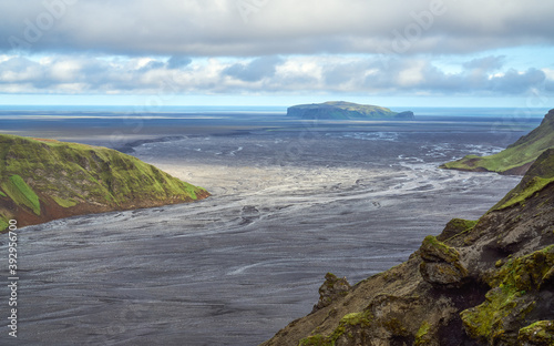 The broad sandy plains of southern Iceland stretch towards the isolated promontory of Hjörleifshöfði, with braided riverbeds and distant mountains.