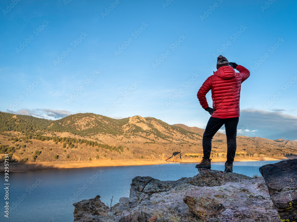 Obraz premium male hiker in a down jacket on a cliff overlooking Horsetooth Reservoir, popular recreation destination for boating, hiking and biking in northern Colorado, fall scenery at sunrise