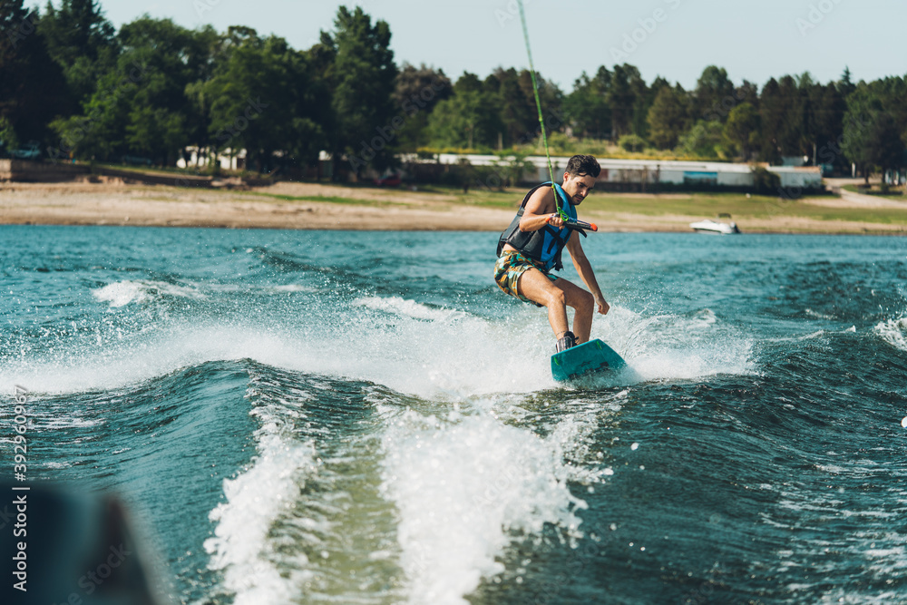 young man doing wakeboarding in a lake whit mountains also doing jumps