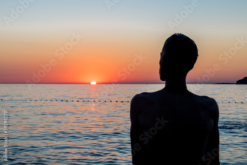 silhouette en contre jour d'un homme face à un coucher de soleil en bord de mer