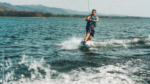 young man doing wakeboarding in a lake whit mountains also doing jumps