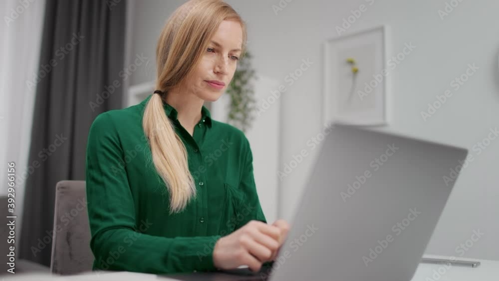 Concentrated woman in green shirt working on modern laptop from home. Female freelancer using portable computer for remote work. Concentrated woman in green shirt working on modern laptop from home. Female freelancer using portable computer for remote work.