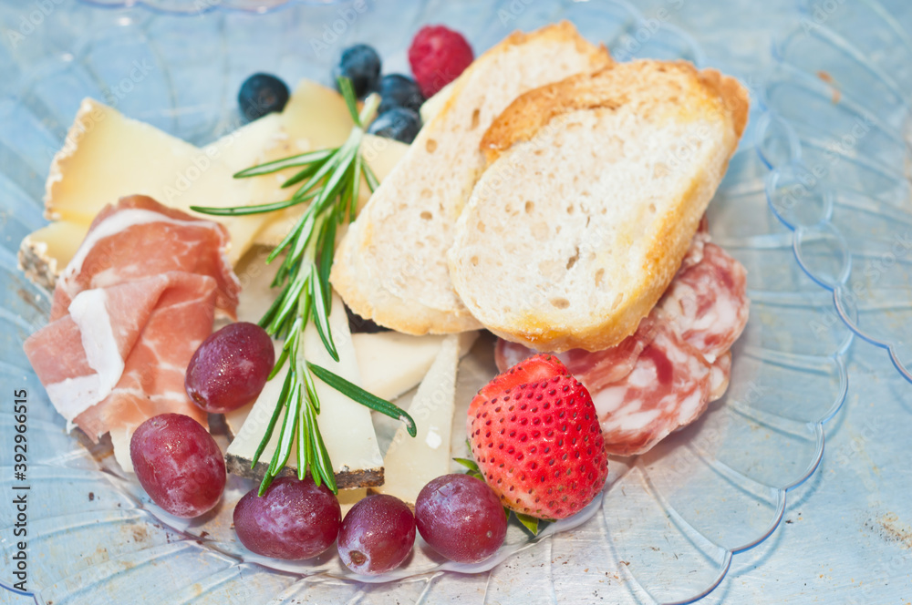 top, front view, close distance of a plate of sliced salami, variety of cheeses, sliced French bread, blueberries, variety of cheese,  food pairings for a French wine tasting event

