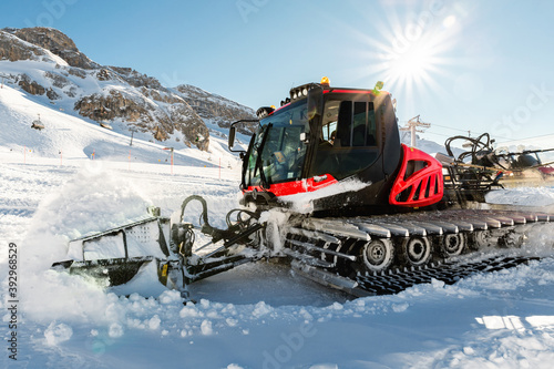Red modern snowcat ratrack with snowplow snow grooming machine preparing ski slope piste hill at alpine skiing winter resort Ischgl in Austria. Heavy machinery mountain equipment track vehicle