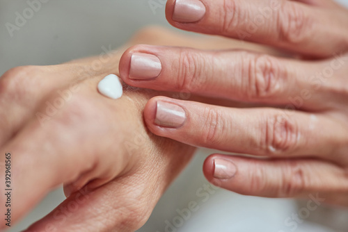 Manicured hands of middle aged woman applying cream