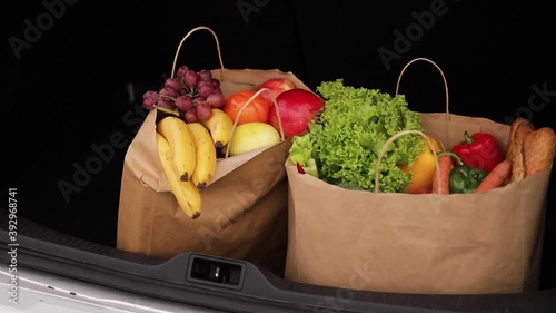 Groceries from a supermarket in a car trunk. Food delivery during quarantine. Cruft Paper eco bags for shopping. Fresh fruits and vegetables, vegan