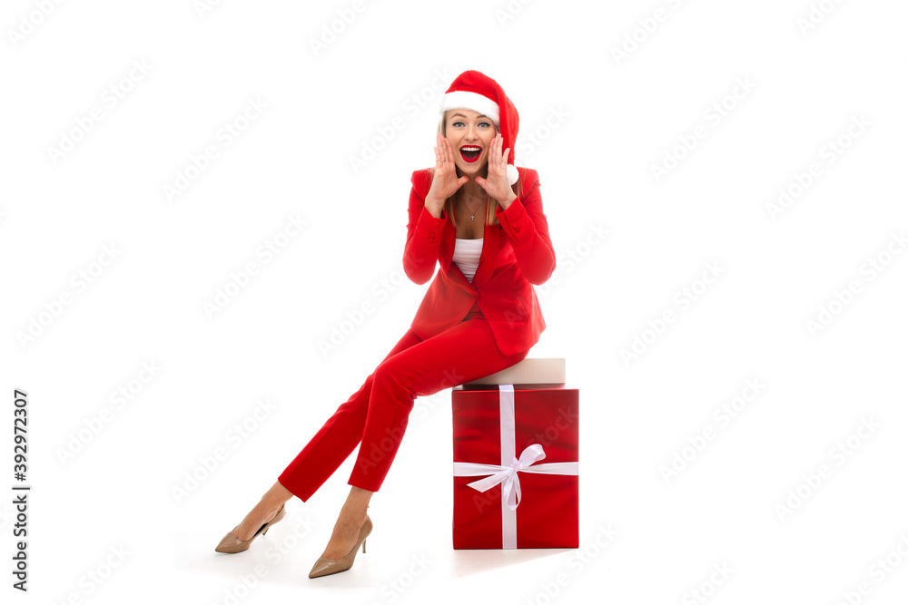 Pretty lady in Santa hat and fancy red costume sitting on wrapped gift box and cupping hands arounf her mouth. Holiday concept Pretty lady in Santa hat and fancy red costume sitting on wrapped gift box and cupping hands arounf her mouth. Holiday concept