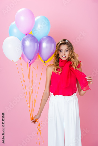elegant confused woman in crown with balloons on pink background