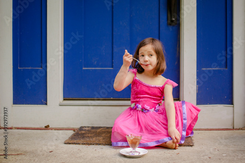 A little girl sits on her front stoop eating chocolate ice cream photo