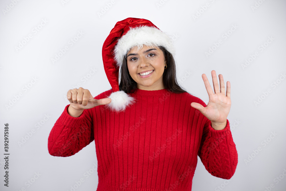 Young beautiful woman wearing a Santa hat over white background showing and pointing up with fingers number six while smiling confident and happy Young beautiful woman wearing a Santa hat over white background showing and pointing up with fingers number six while smiling confident and happy