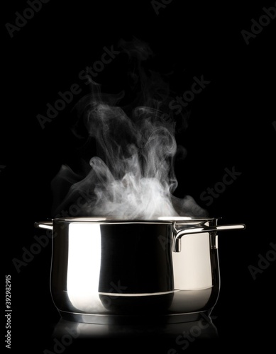 Open stainless steel cooking pot with steam over black background, cooking or kitchen utensil
