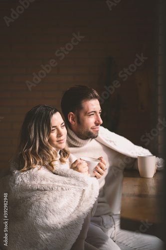 Young couple in love enjoying coffee on a sunny winter sunday morning by the window at home