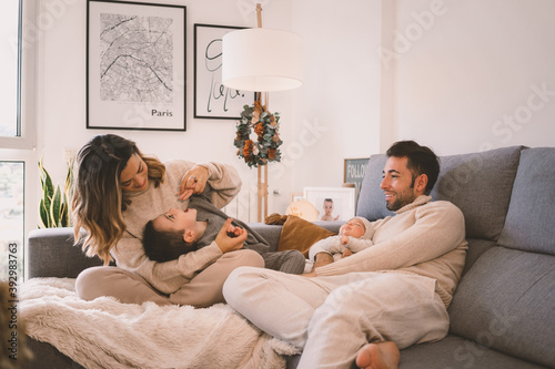 Young family with their little one and their baby enjoying and playing on the sofa at home during Christmas