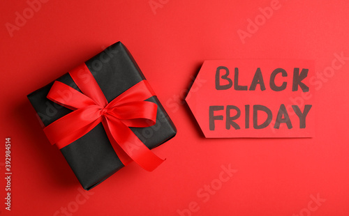 Tag with phrase Black Friday and gift box on red background, flat lay