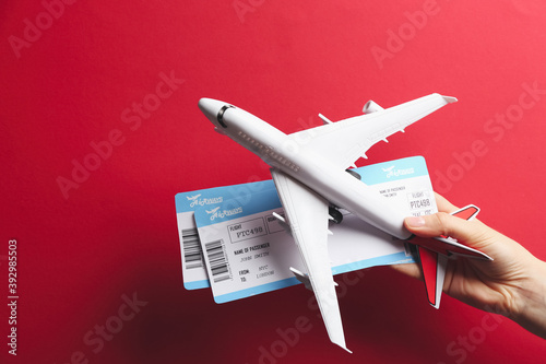 Woman holding toy airplane and tickets on red background, closeup