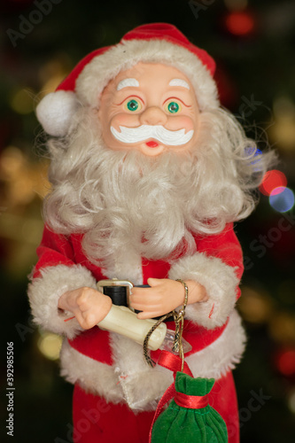 Santa Claus doll with candle in hand and small green gift bag and bokeh in the background