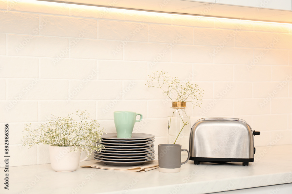 Modern toaster, crockery and flowers on counter in kitchen Modern toaster, crockery and flowers on counter in kitchen