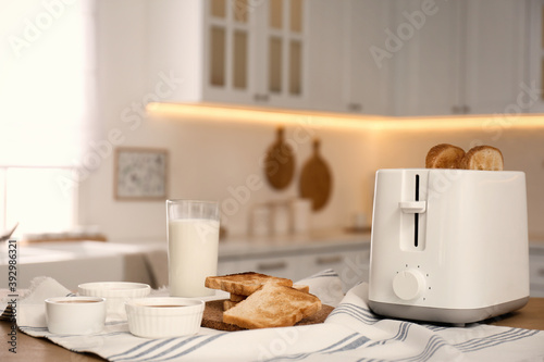 Modern toaster and tasty breakfast on wooden table in kitchen