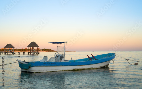 Принти на полотні Small fishing boat anchored in calm waters at sunset with a thatched palapa in the background in Riviera Maya, Mexico