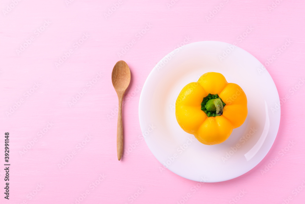 Fototapeta Yellow bell pepper on white plate with wooden spoon on pink background, Top view