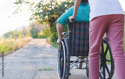 Fotografia Rear view of disabled handicapped man in wheelchair and care helper walking in park