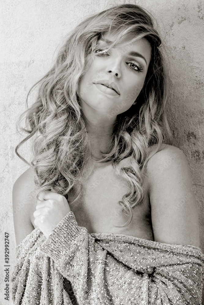 Black and white portrait of beautiful sexy blonde girl with long hair wearing pullover, sensual posing on scratched wall.