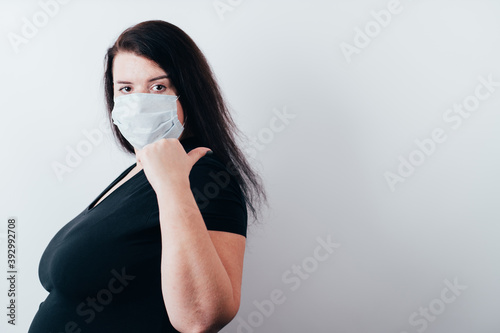 Woman in medical mask pointing thumb on copy space