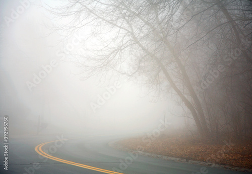 Foggy road with bright yellow lines curving and disappearing into a thick mist