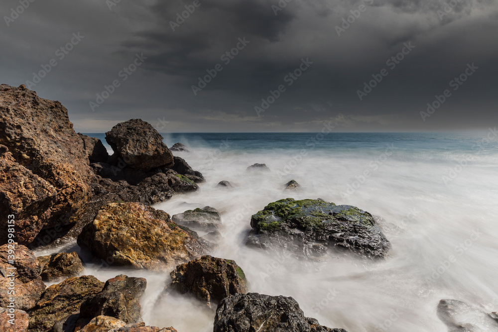 Pacific coast rocks and waves with storm sky at Point Dume in Malibu, California.