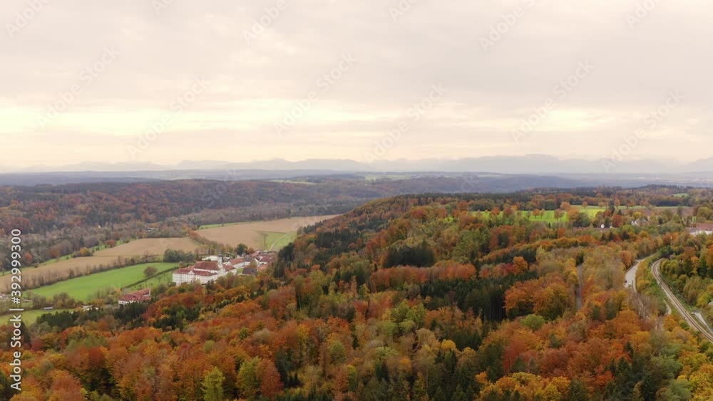 Flying forward by a drone over a autumn colored forest with the white architecture of an bavarian monastery in focus at the left side Flying forward by a drone over a autumn colored forest with the white architecture of an bavarian monastery in focus at the left side