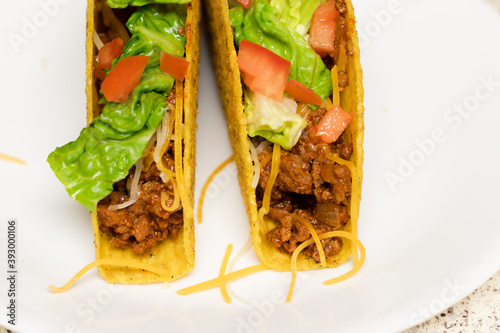 Two tacos on a white plate topped with lettuce, tomato, and cheese, ready to be served.