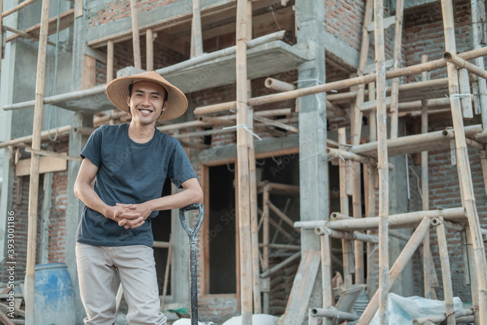 cropped image of mason wearing a smiling hat while standing with a shovel at the unfinished construction of a house cropped image of mason wearing a smiling hat while standing with a shovel at the unfinished construction of a house
