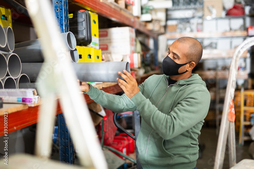 Craftsman in protective mask selects plastic plumbing pipes in a hardware store