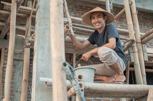 construction workers smile at the camera as they squat on the bamboo planks for wall stucco in an unfinished house