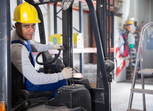 Skilled hispanic worker of building materials warehouse working on forklift truck..