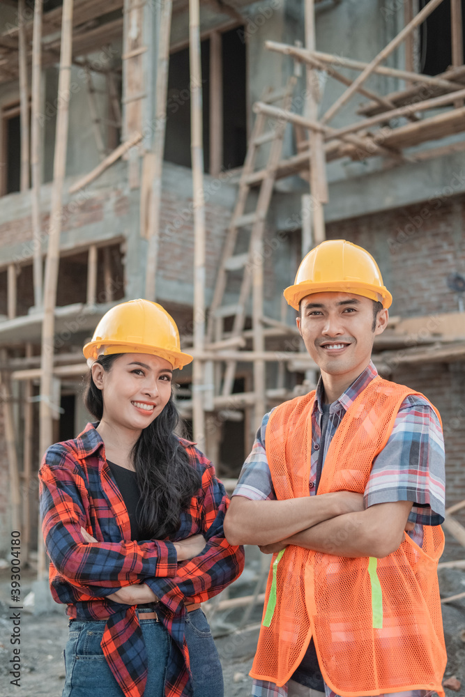 male and female contractors standing with crossed hands smiling at the camera wearing safety helmets against the background of the unfinished building male and female contractors standing with crossed hands smiling at the camera wearing safety helmets against the background of the unfinished building
