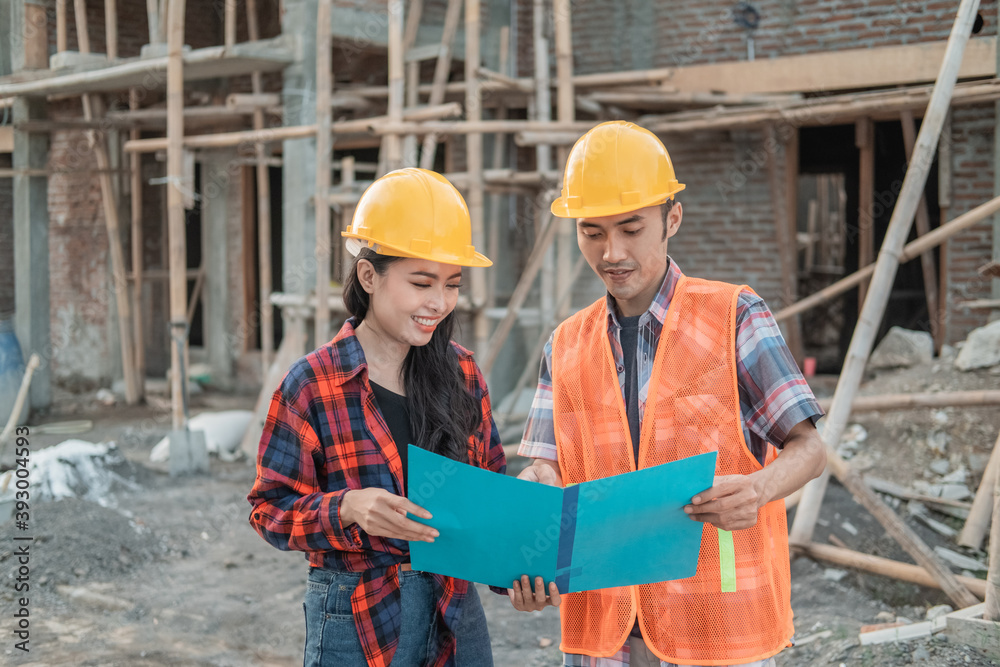 male and female contractors standing holding sketchbooks of drawings wearing safety helmets against the background of the unfinished building male and female contractors standing holding sketchbooks of drawings wearing safety helmets against the background of the unfinished building