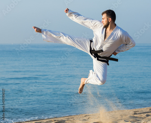 Positive man doing karate at ocean quay in dawn