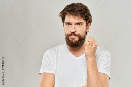 A man in a white t-shirt with a beard emotions displeased facial expression light background