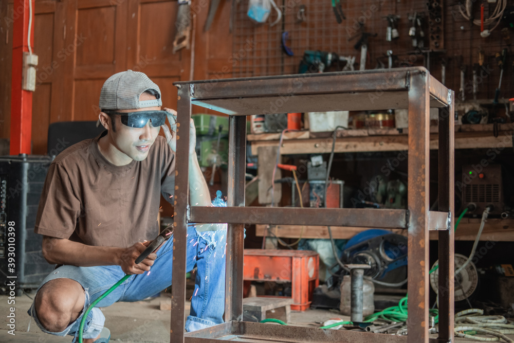 Squat welder prepares the equipment to make iron racks in the welding workshop Squat welder prepares the equipment to make iron racks in the welding workshop