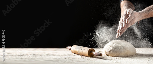 Obraz na plátně White flour flying into air as pastry chef in white suit slams ball dough on white powder covered table