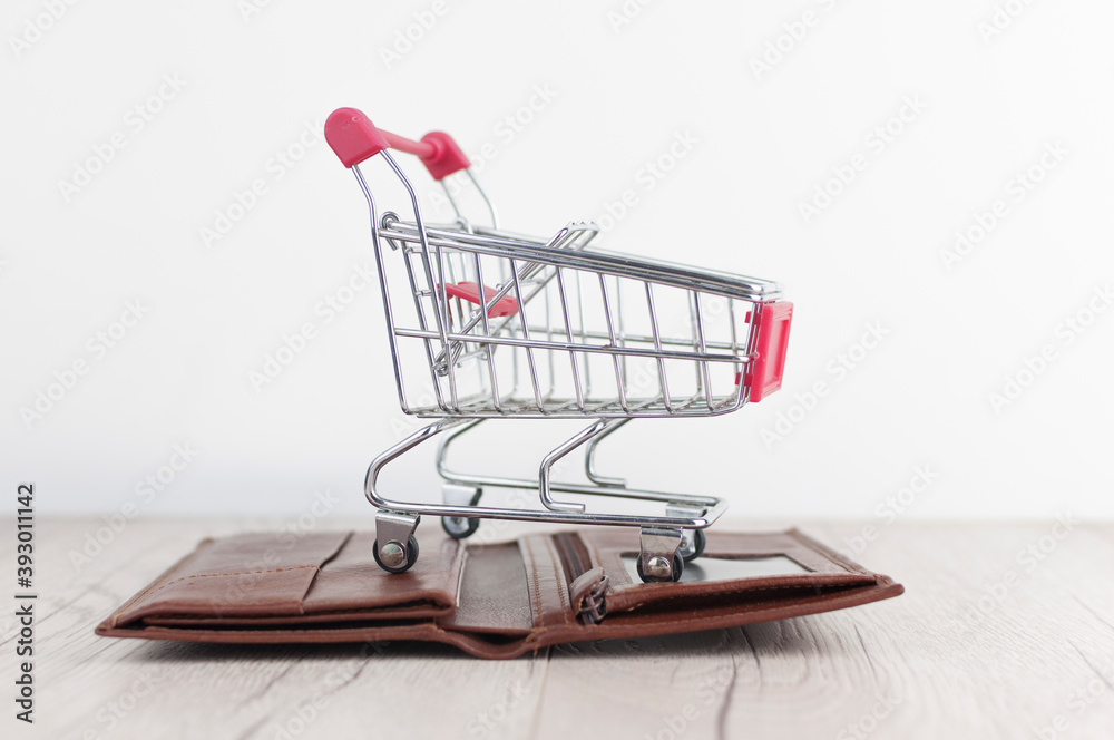open leather wallet and mini shopping cart on white wood background open leather wallet and mini shopping cart on white wood background