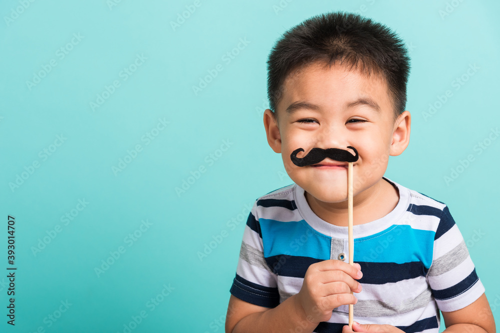 Funny happy hipster kid holding black mustache props for the photo booth close face, studio shot isolated on a blue background, Men health awareness, Prostate Cancer Awareness Funny happy hipster kid holding black mustache props for the photo booth close face, studio shot isolated on a blue background, Men health awareness, Prostate Cancer Awareness
